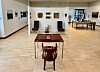 Bright art gallery with framed works, a central table, and a sculptural chair in the foreground.